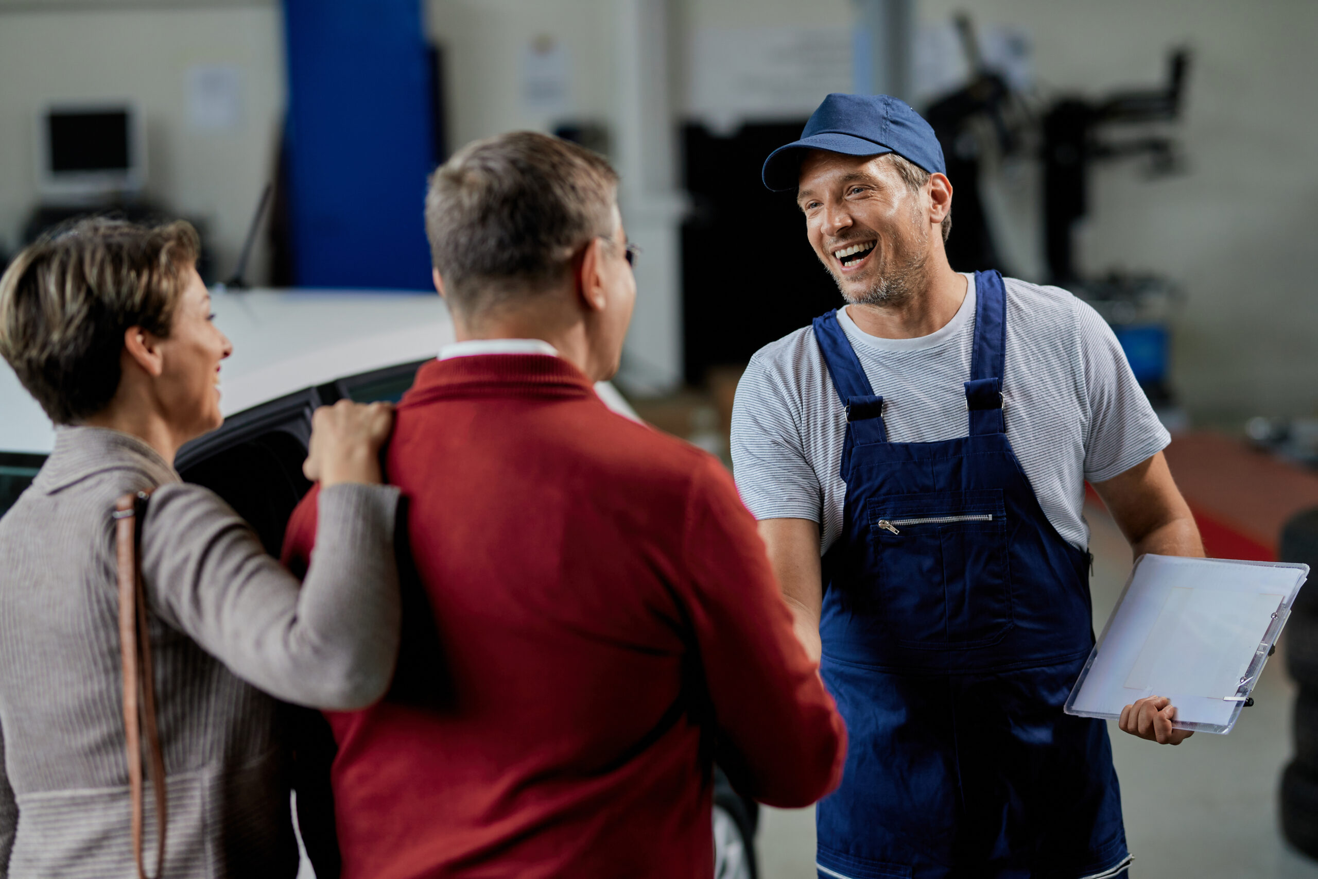 About happy car mechanic greeting a couple in auto repair shop.