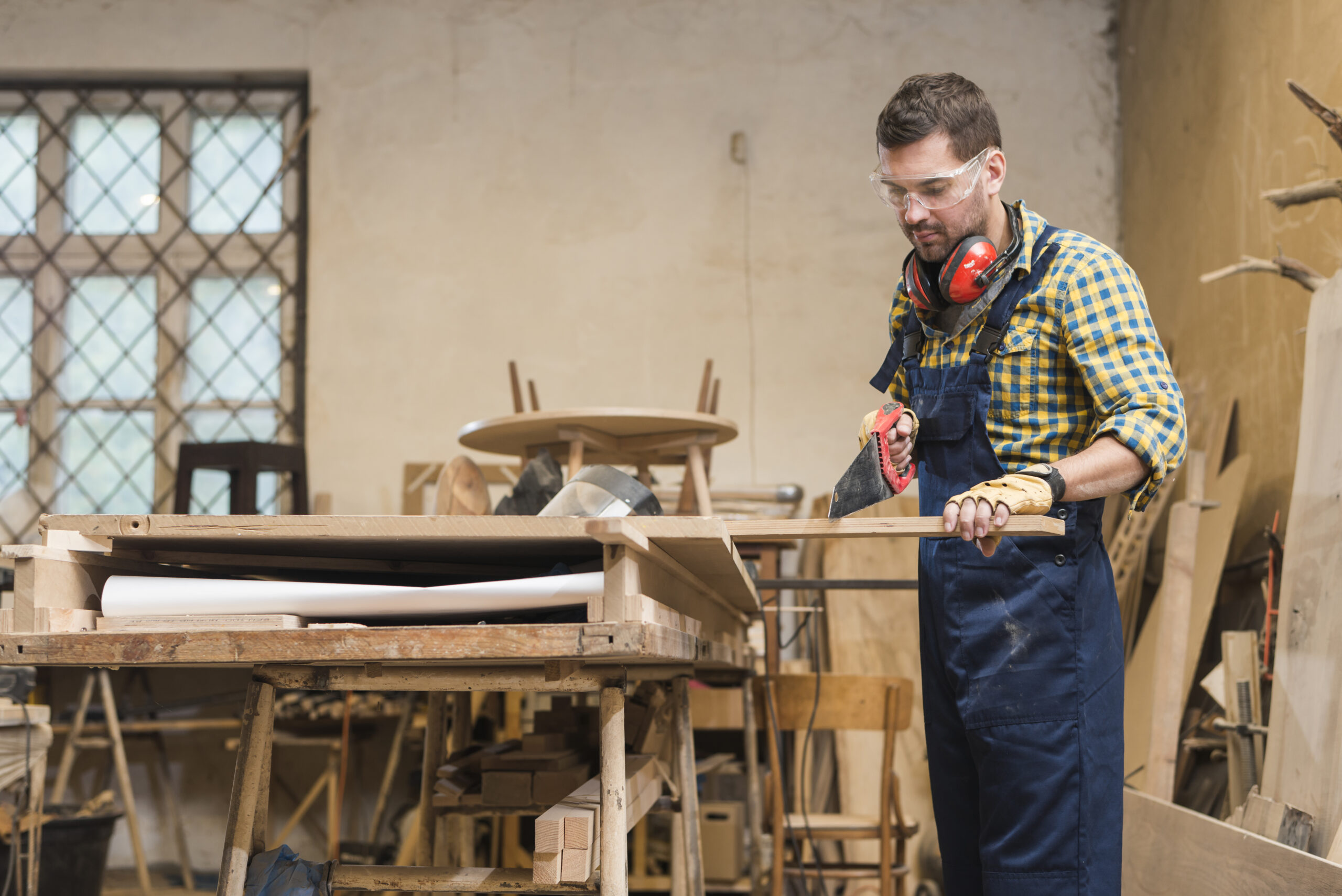 Carpentry Services professional carpenter cutting wooden plank with handsaw workshop